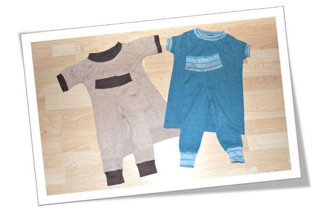 Zwei Kinderstrampler liegen nebeneinander auf hellem Holzfußboden.