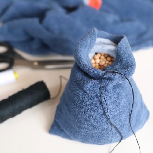 Selbstgenähtes blaues Stoffbeutelchen mit Perlen, Nadel und Faden daneben.