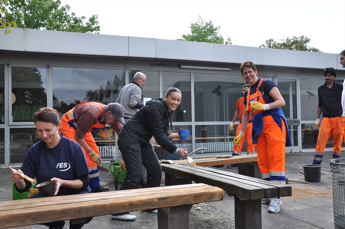 Mehrere Personen in orangefarbener Arbeitskleidung helfen bei einer Freiluftaktion