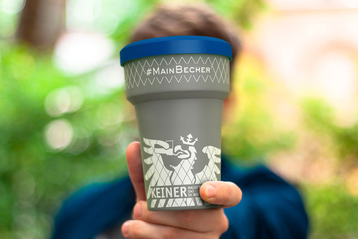 Person hält MainBecher mit Logo in Kamera